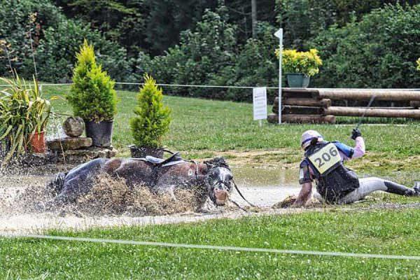 Horse and event rider fall in the water obstacle at a competition