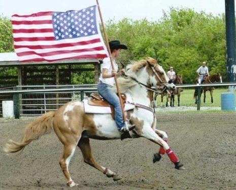 A western rider carries the flag while her horse fights against the pressure on his bit.