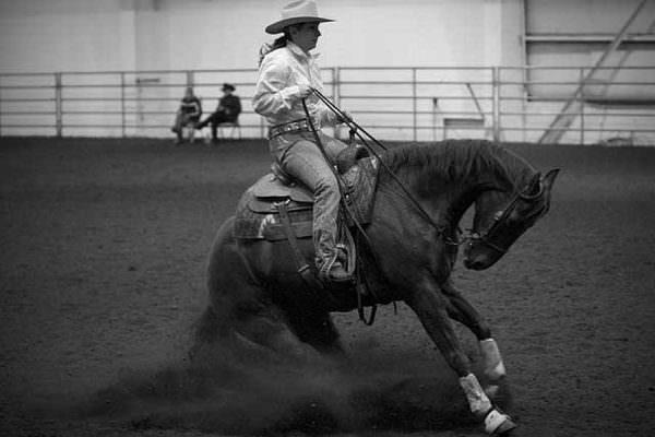 A reining horse is pulled to a sliding stop and hyperflexed by a cowgirl.
