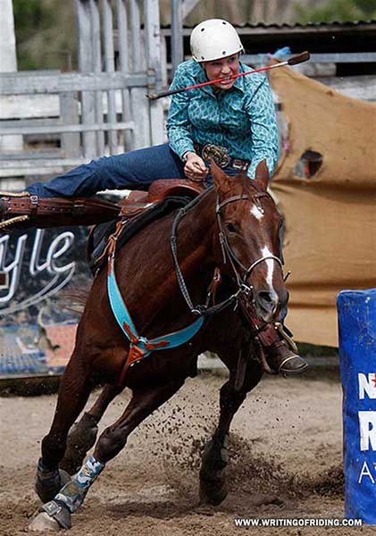 Whip in mouth, this barrel racer is serious about driving her horse forwards with wildly kicking legs.