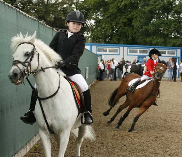 Two children riding at a competition show bad habits and over-the-top tack.
